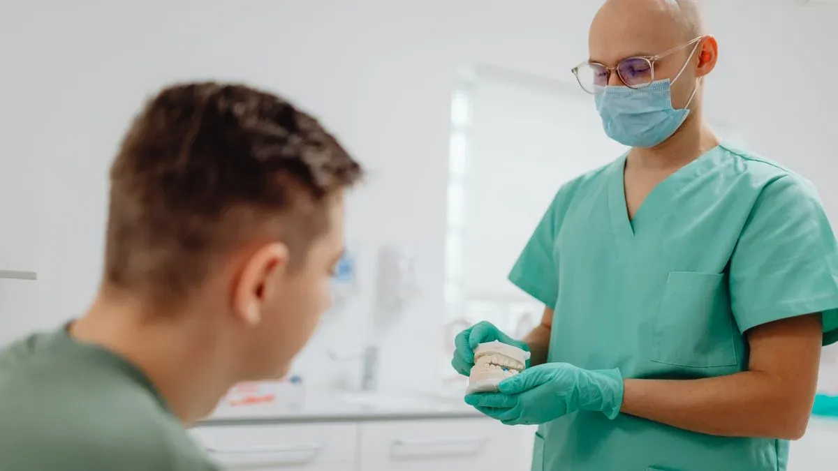 Dentist in scrubs holding a dental model and explaining treatment options to a patient in a clinic
