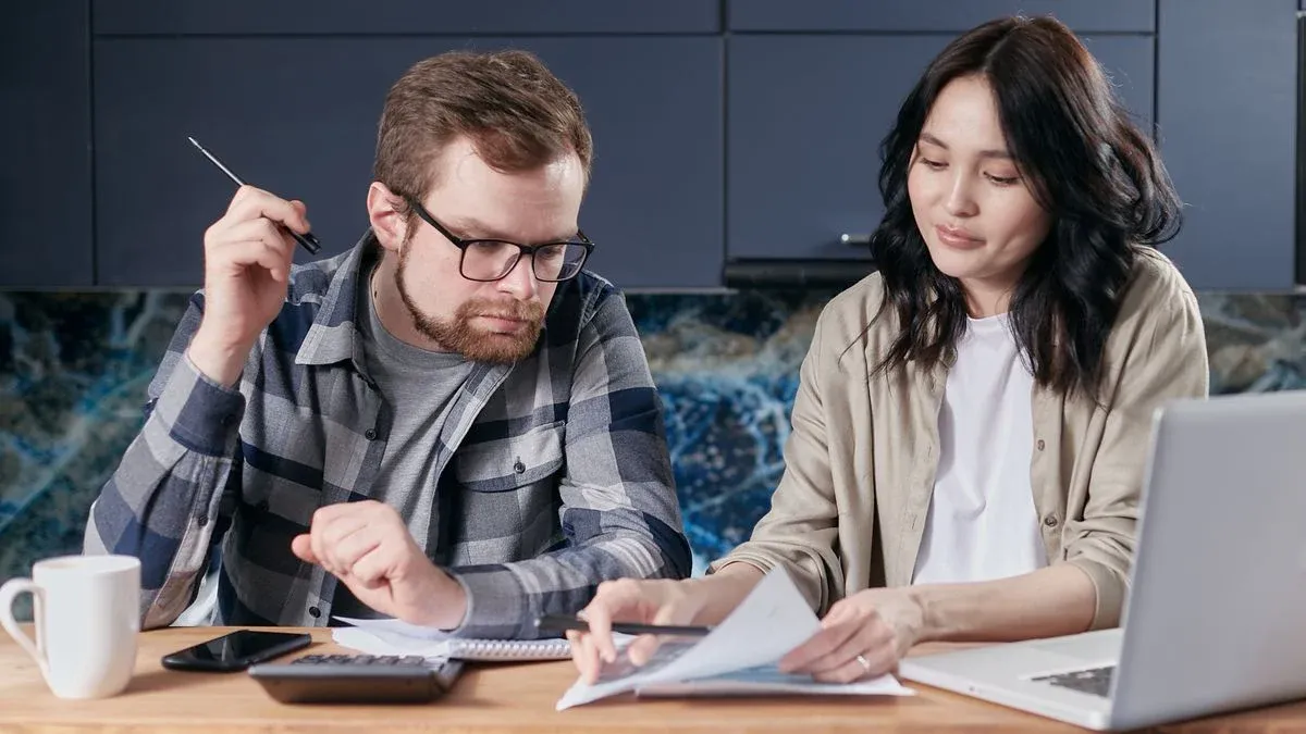 A couple sitting at a kitchen table reviewing bills and calculating expenses together