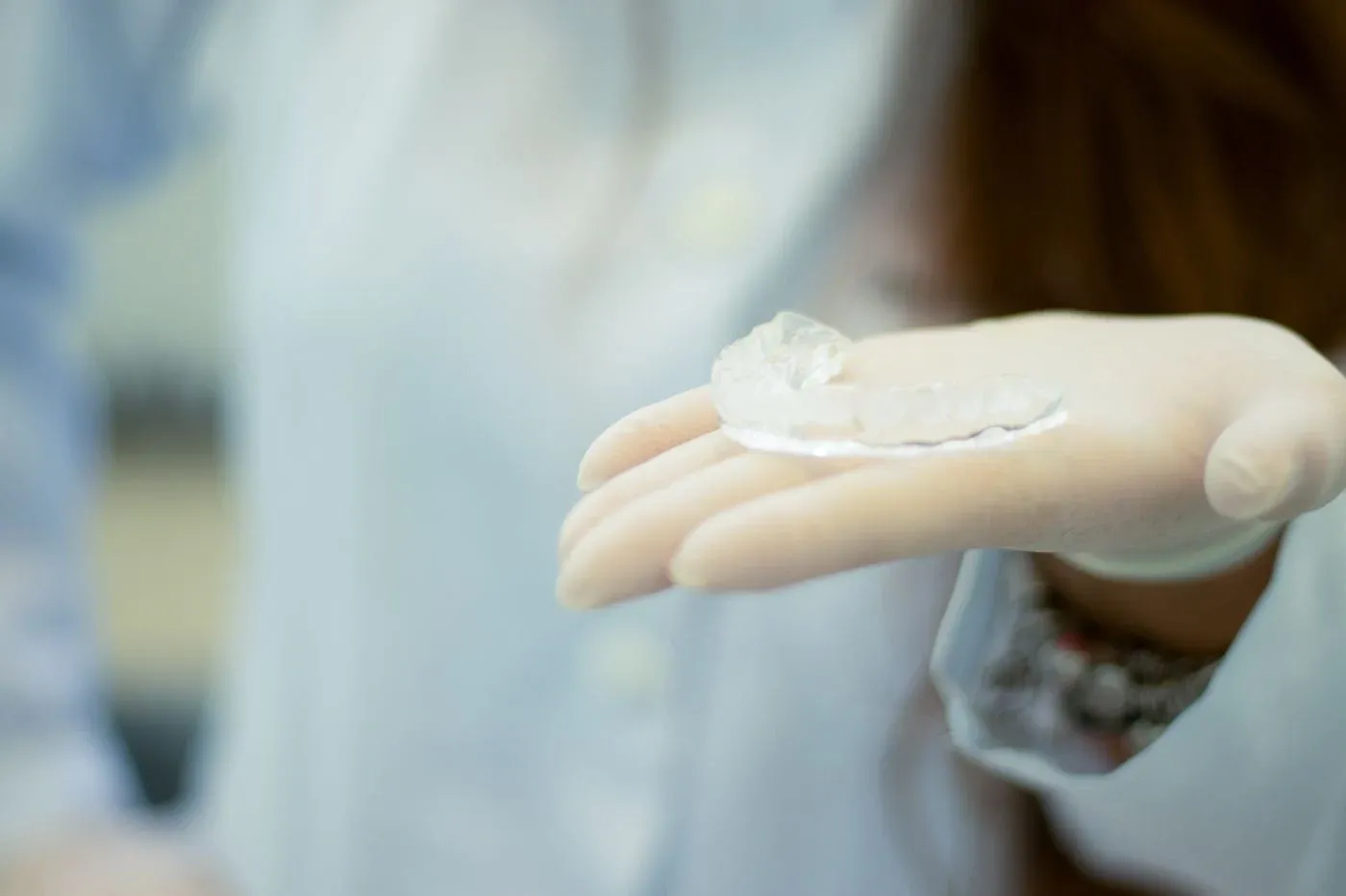 A gloved hand holding up a clear custom dental night guard