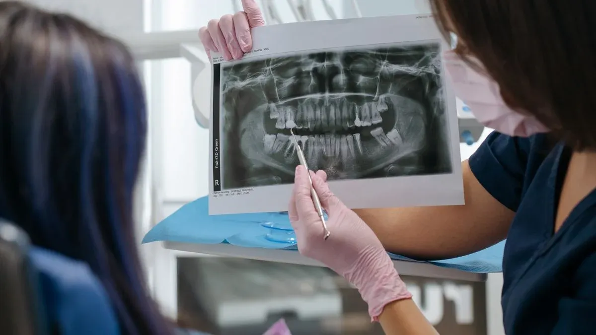 Dentist holding up a panoramic dental X-ray and pointing at the lower teeth with a dental instrument while a patient looks on