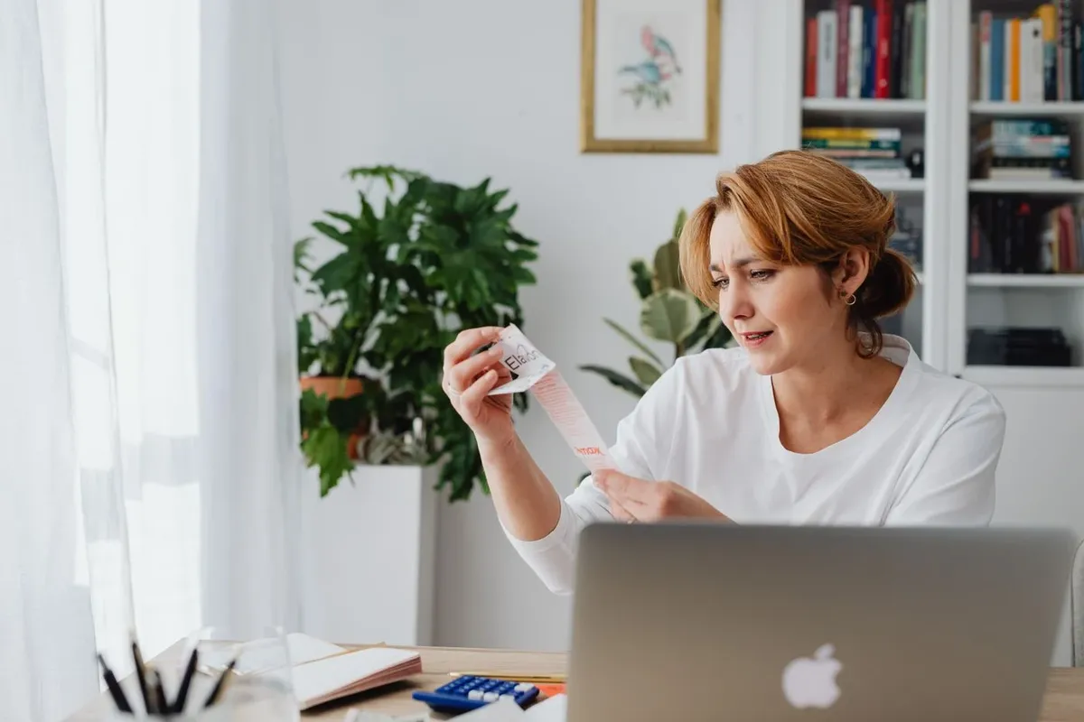 A woman at home examining a long itemized receipt with a concerned expression