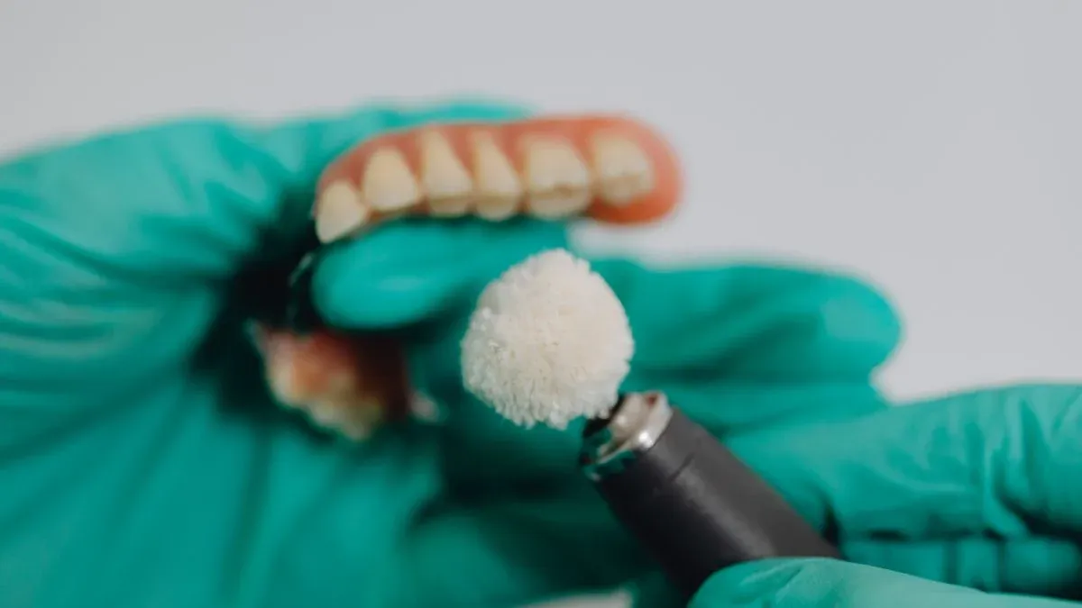 A dental professional in green gloves polishing a set of dentures