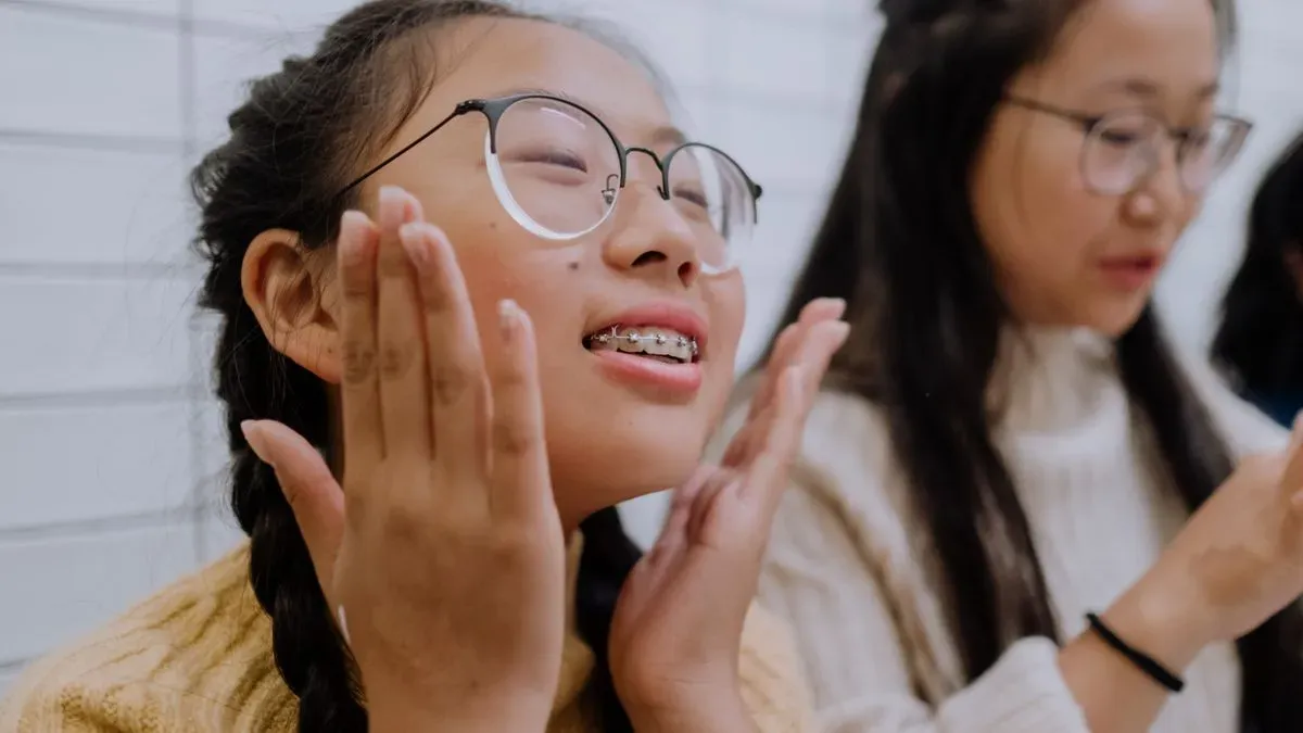 A smiling teenage girl with glasses and braces sitting next to a friend