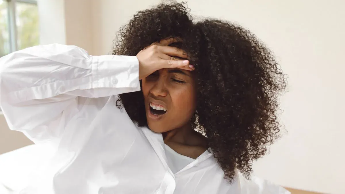 A young woman in a white shirt waking up and holding her head in discomfort