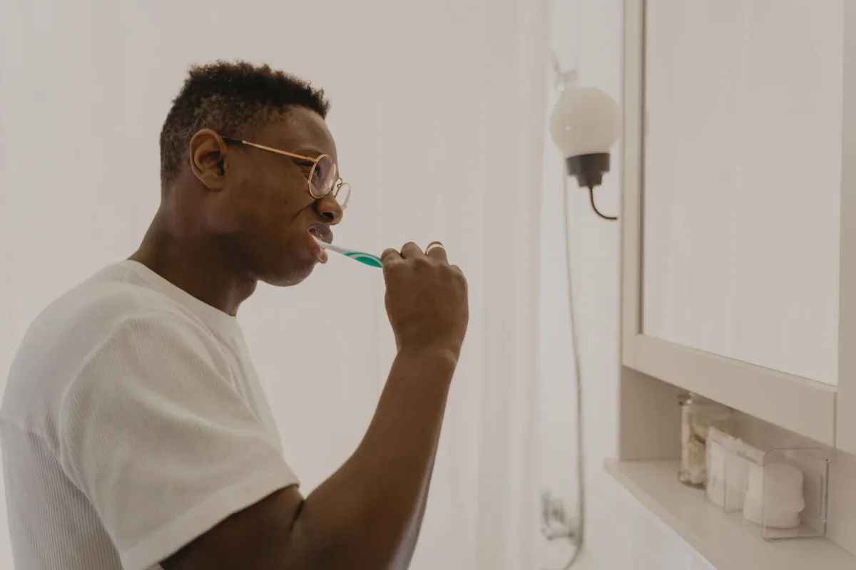 A man brushing his teeth at a bathroom sink as part of a daily oral care routine