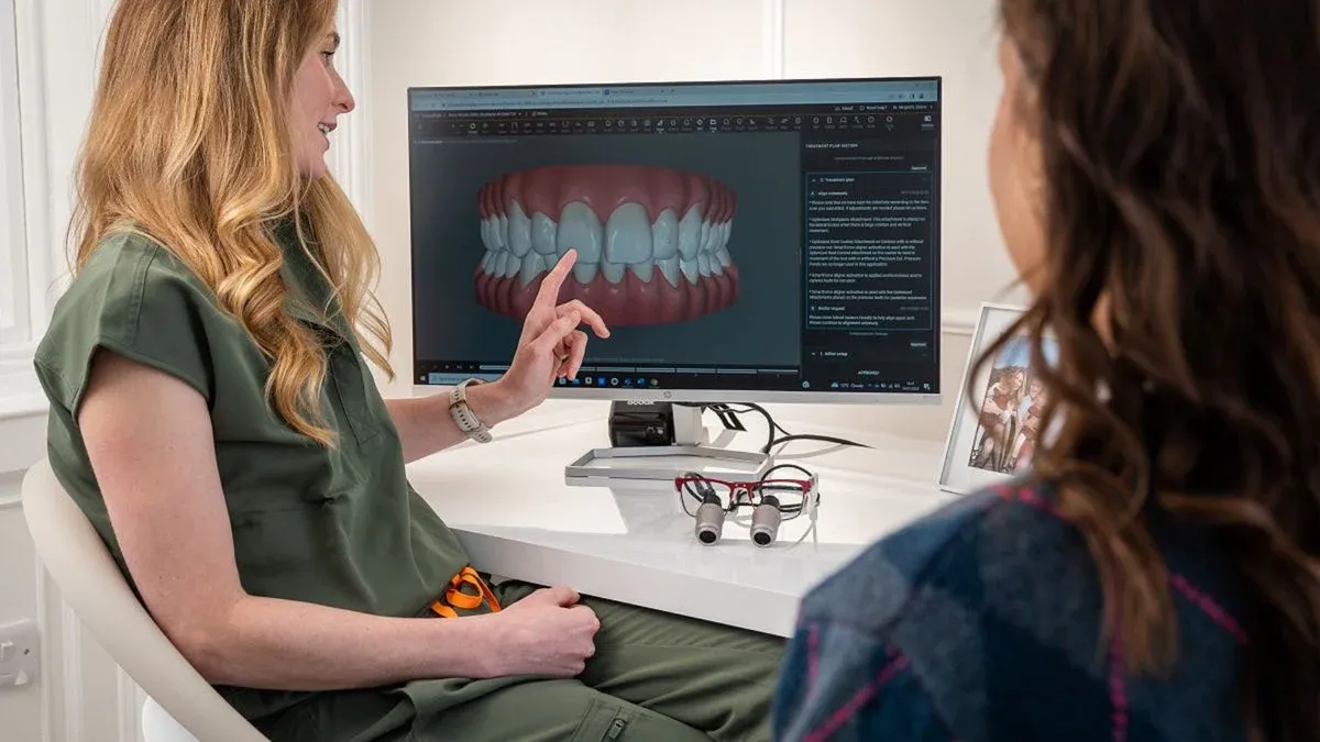 Dentist pointing to a 3D scan of a patient's teeth on a monitor while explaining treatment to a patient