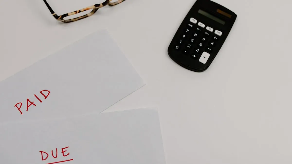 Two sheets of paper marked Paid and Due beside a calculator and a pair of glasses