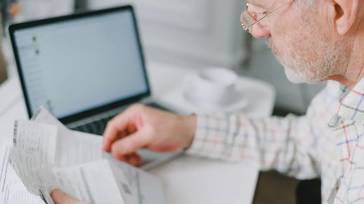 An older adult compares dental plan documents beside a laptop at home