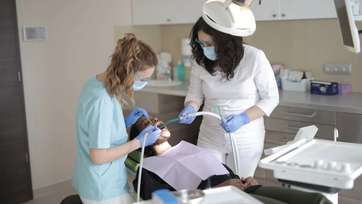 A dentist examining a patient's teeth with an assistant present, representing care covered under an individual dental plan