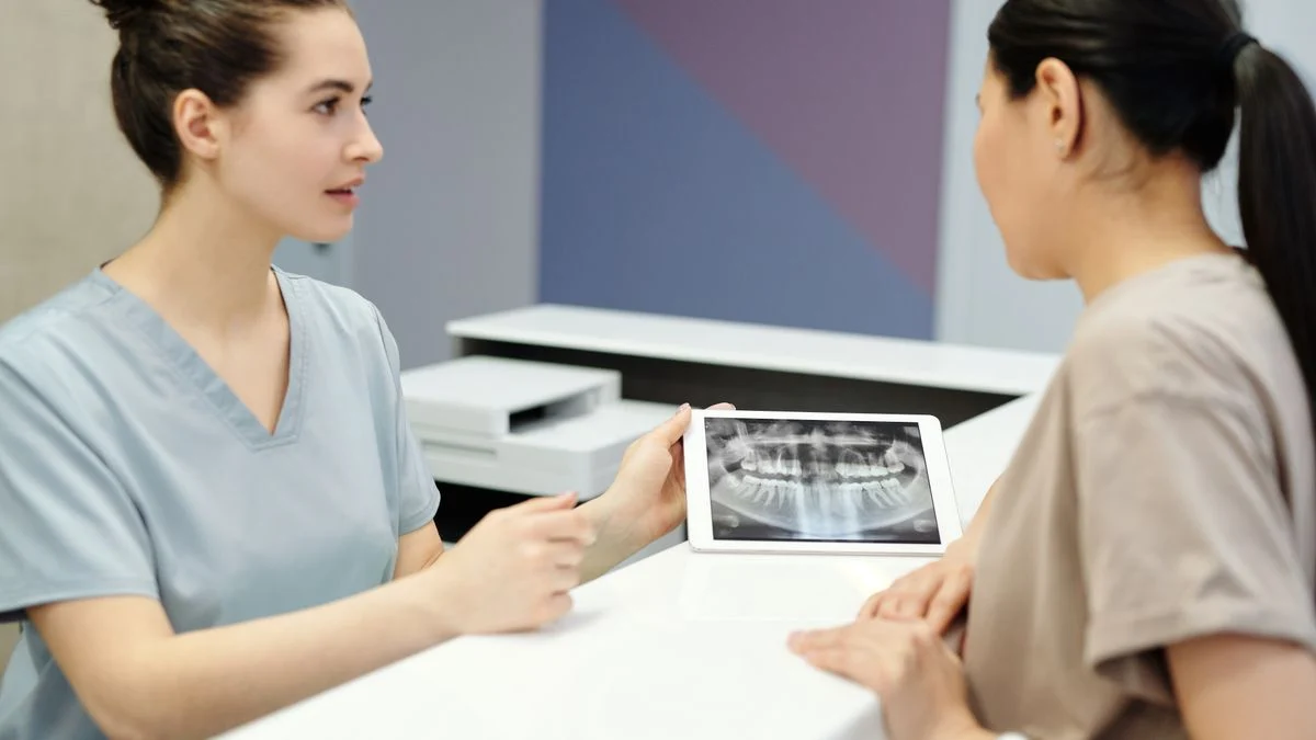 Dentist reviewing a dental X-ray with a patient to identify a pre-existing condition Dentist showing a patient their dental X-ray on a tablet during a pre-existing condition consultation