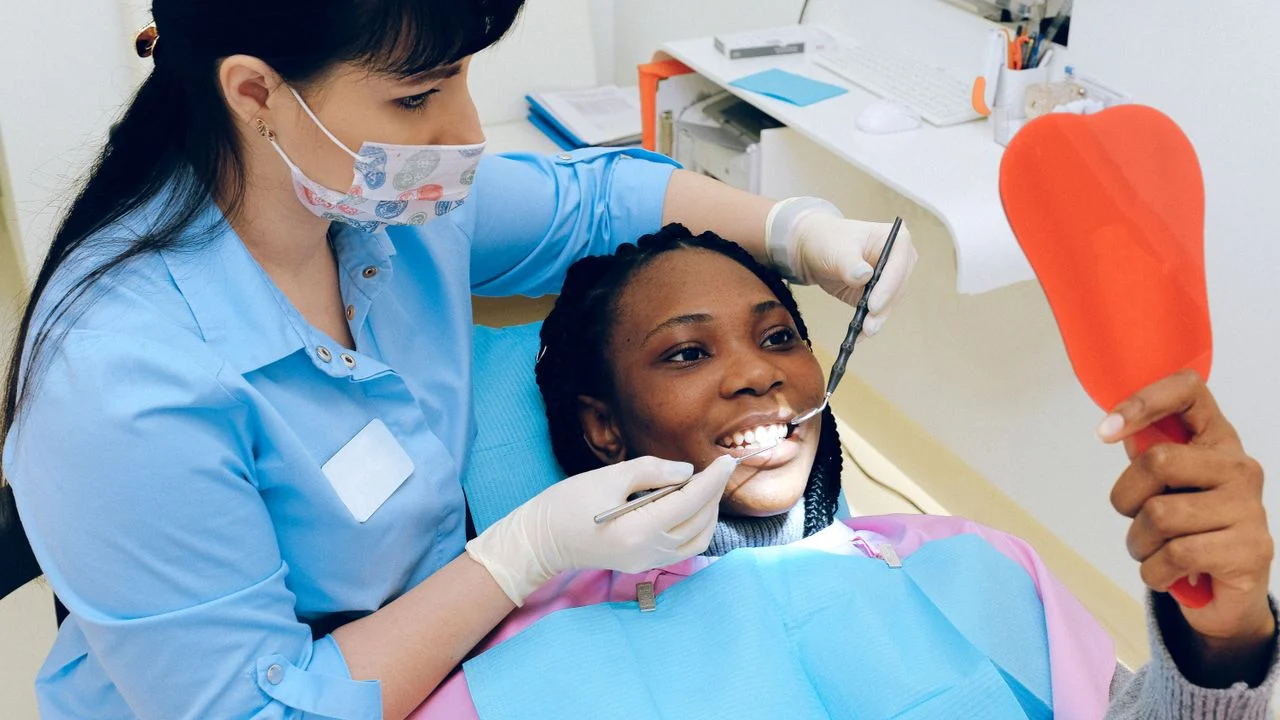 Dentist in blue scrubs examining a smiling patient at a participating dental office — choosing an in-network provider is key to maximizing discount plan or insurance benefits