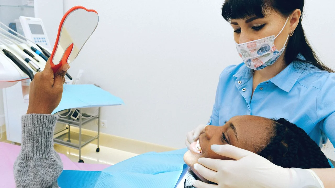 Child patient at dentist holding tooth-shaped mirror during routine checkup covered under a family dental insurance plan