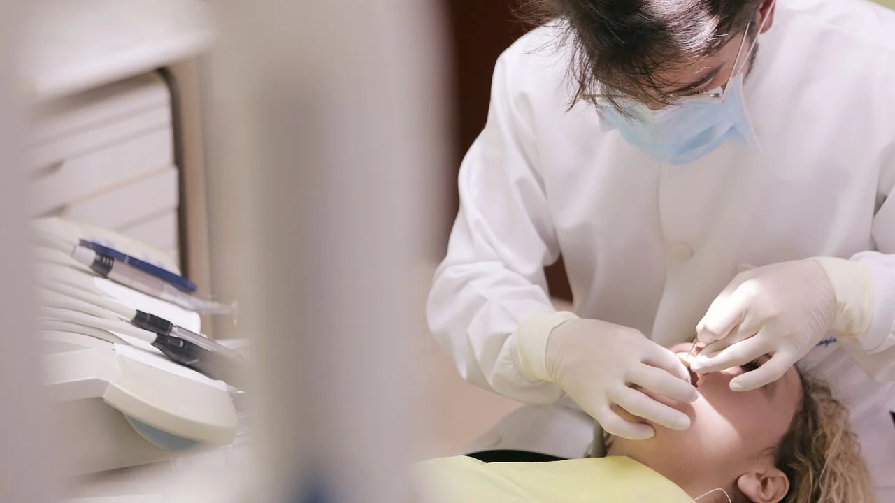 Dentist in white coat and mask examining a patient at a dental office — choosing an in-network provider reduces out-of-pocket costs for family dental insurance holders