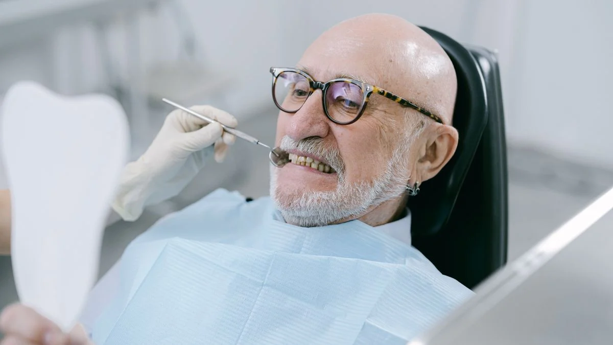 Older man in a dental chair examining his teeth, relevant to Medicare dental coverage