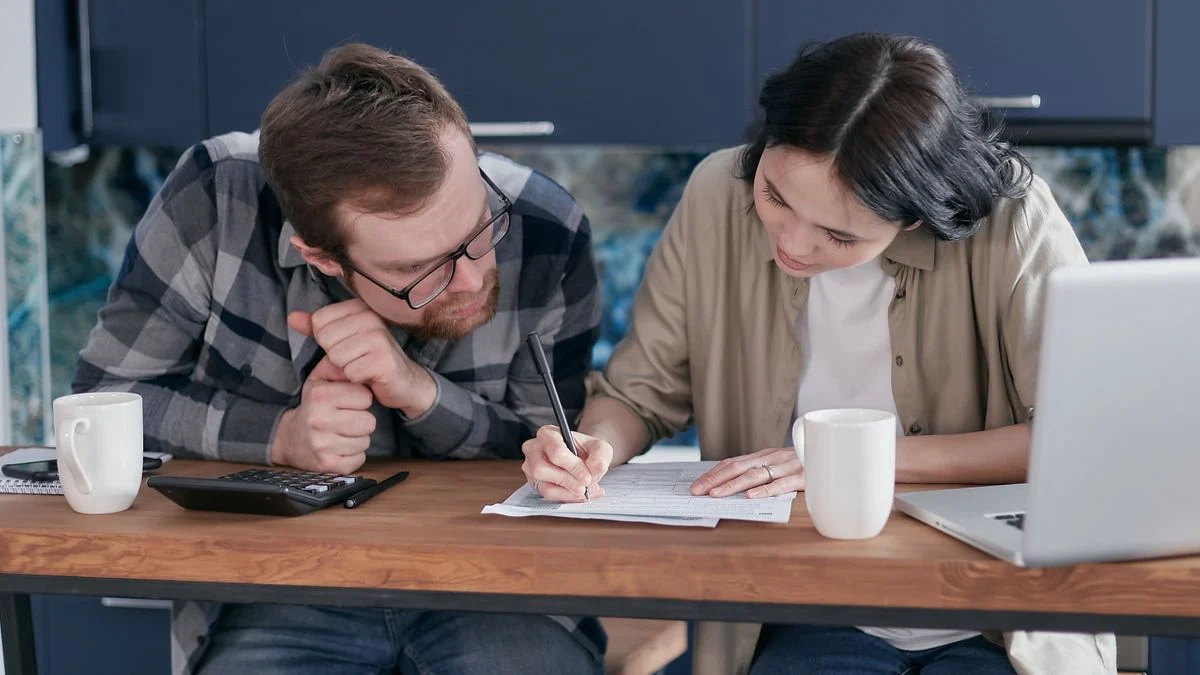 A couple reviewing financial documents together at a kitchen table with a laptop and calculator, comparing dental insurance costs for their family