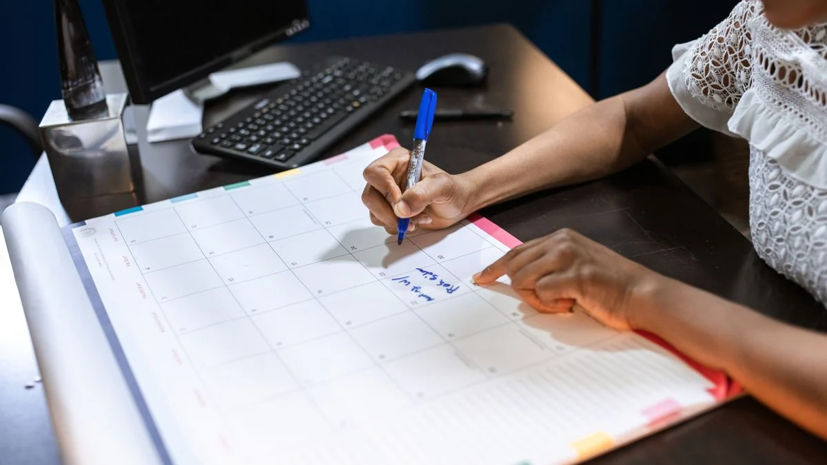 Person writing notes on a desk calendar while tracking dental insurance enrollment dates