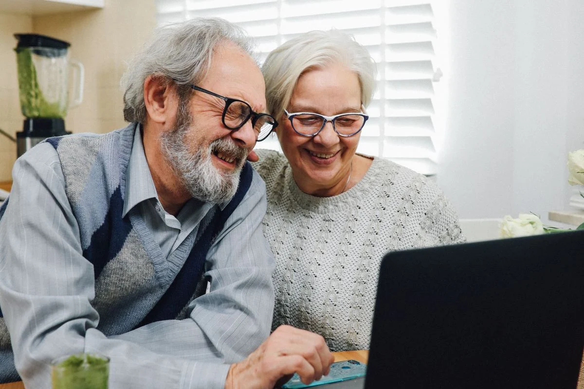 Senior couple smiling while using a laptop together Senior couple smiling while researching dental insurance options on a laptop