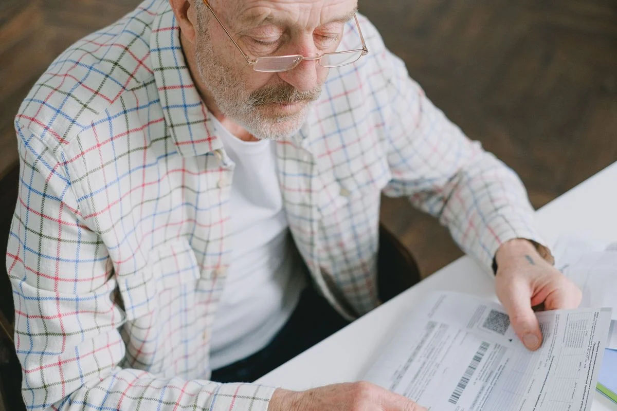 Senior man reviewing dental insurance documents at home through reading glasses