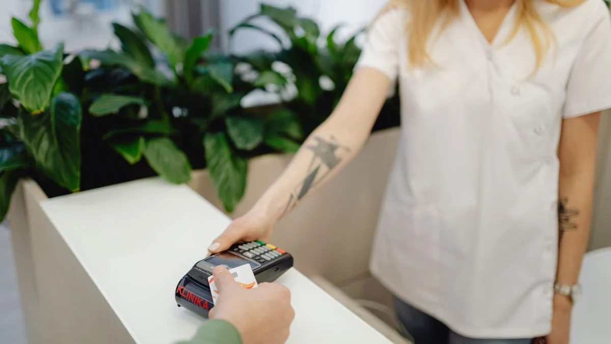 Clinic staff member assisting a patient with a card payment, representing the deductible paid before benefits begin