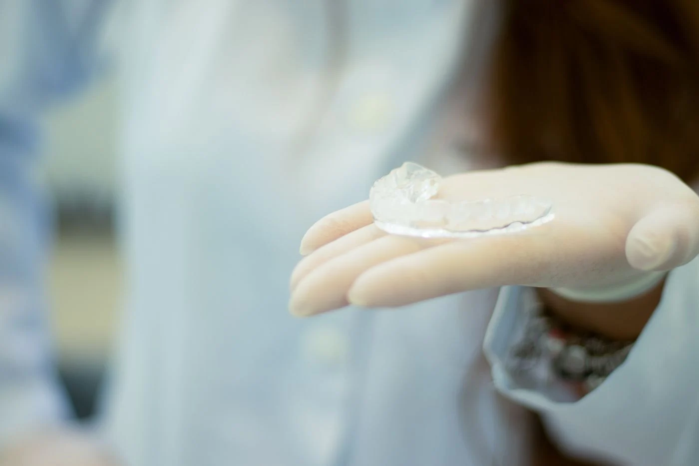Clear custom dental night guard held by a dentist A dentist holds a clear custom night guard in a gloved hand in a clinical setting