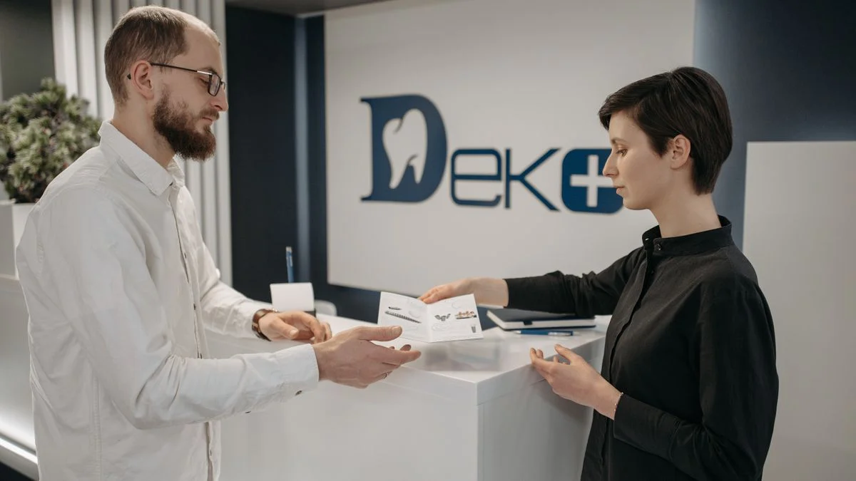 Patient and receptionist exchanging insurance paperwork at a modern dental clinic front desk, representing network and referral rules