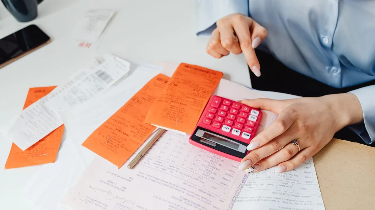 Woman calculating expenses with receipts and a calculator at a desk while working out a monthly dental premium