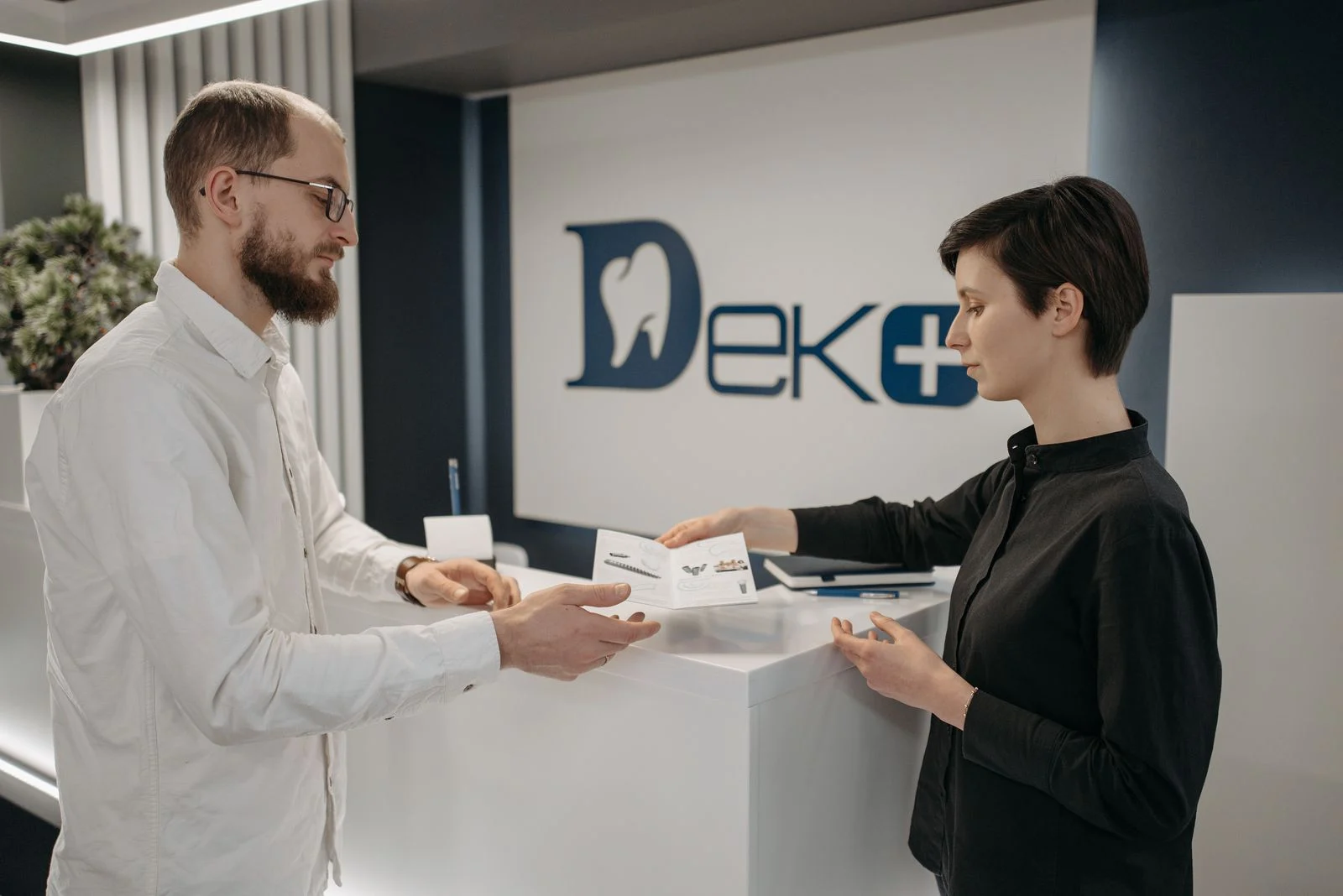 Exchanging paperwork at a dental clinic front desk to enroll in a private dental plan Man and woman exchanging enrollment paperwork at a dental clinic front desk