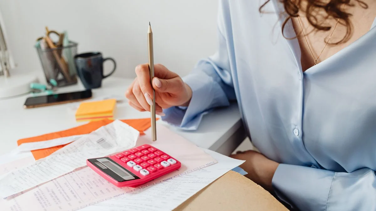 Woman calculating expenses with a calculator and paperwork at her desk while working out whether a dental plan pays for itself