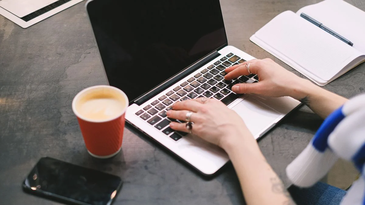 Freelancer working on a laptop with coffee and a notepad, representing a self-employed worker paying full premiums alone