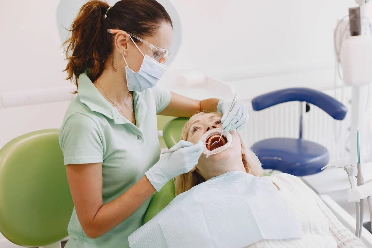 A female dentist examines a senior woman's teeth during a dental clinic checkup.