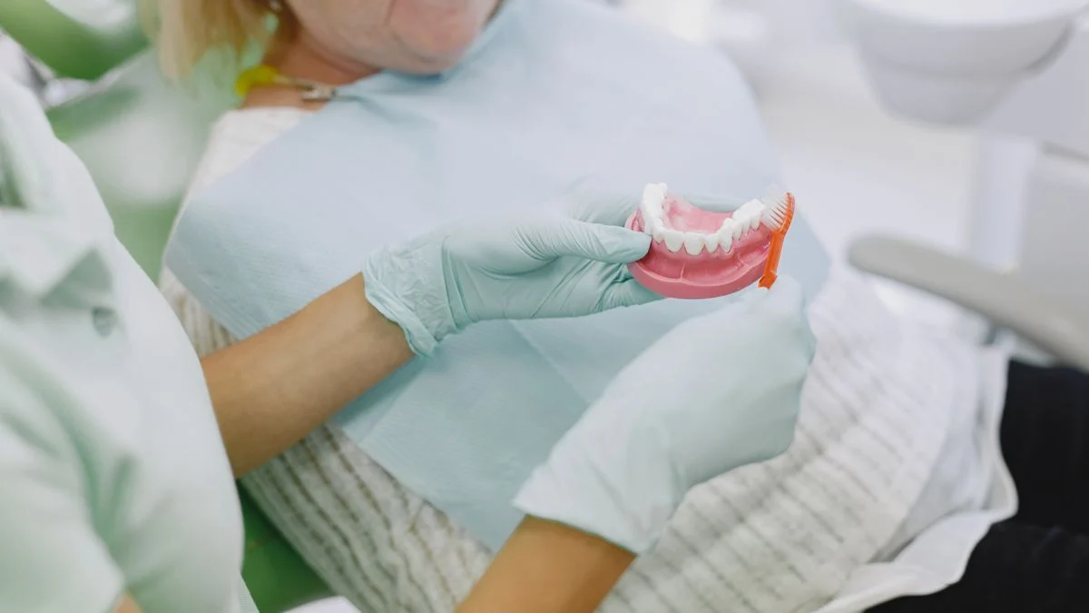 Senior woman learns denture care as part of her dental insurance plan, guided by a dental professional.