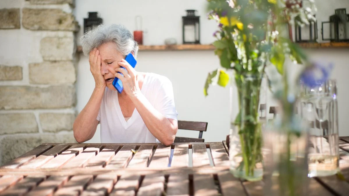 An elderly woman looks distressed while holding a cellphone outdoors, reflecting the frustration of a failed directory search.