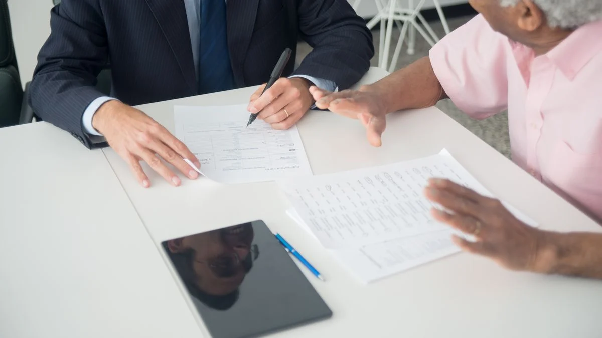 An elderly client and a consultant discussing dental insurance plan documents at an office table.