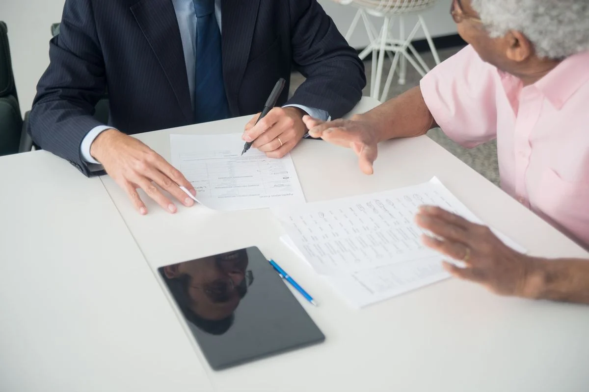 An elderly client reviews insurance documents with a consultant at an office table.