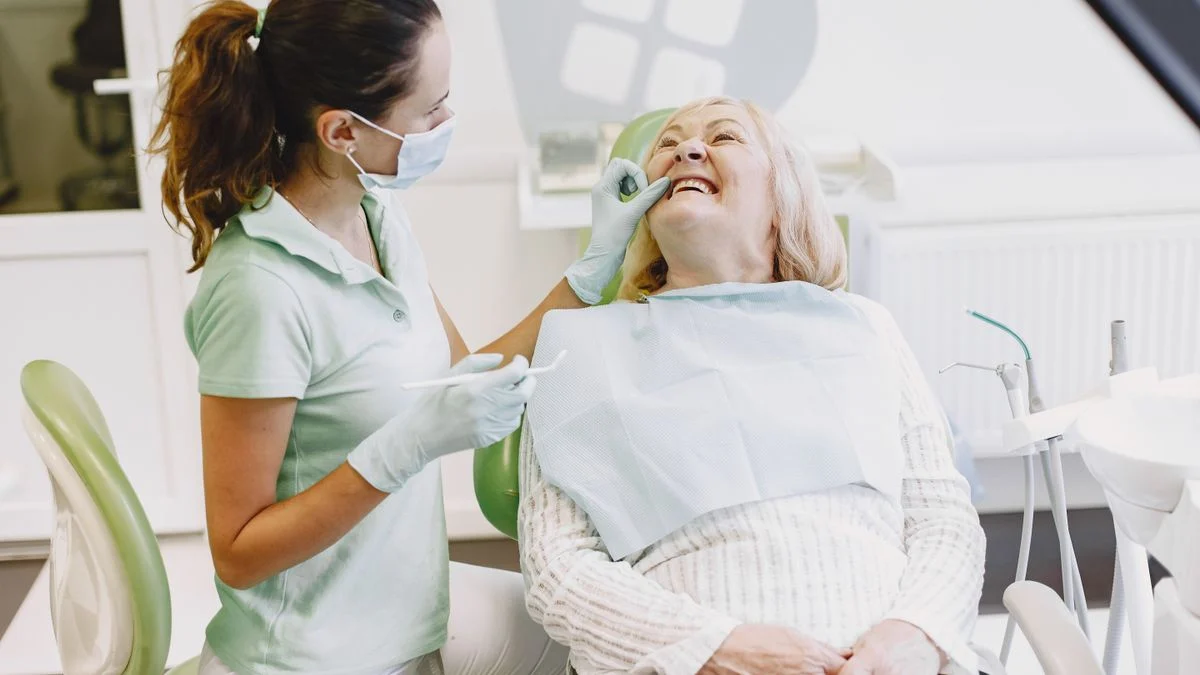 Female dentist examining a smiling senior woman in a dental office, representing routine preventive care for older adults