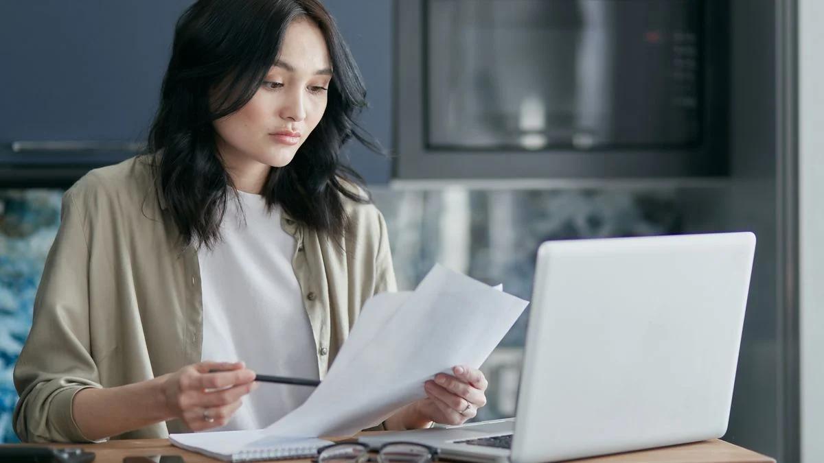 Self-employed woman at a kitchen table comparing dental plan documents on a laptop before choosing a Spirit Dental tier