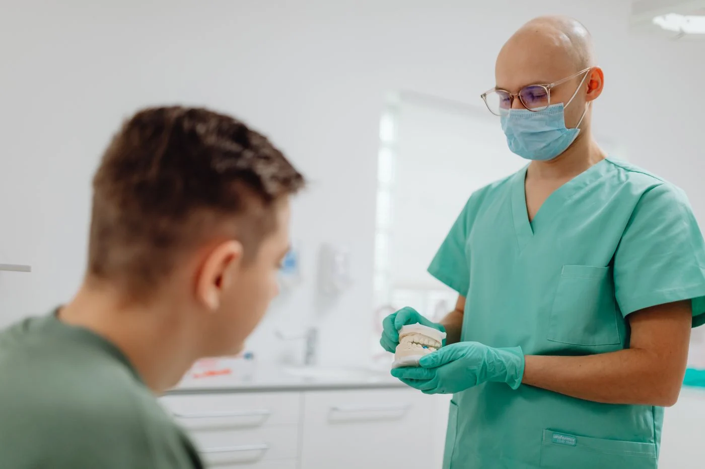 A dentist in scrubs explaining a treatment plan to a seated patient in an office