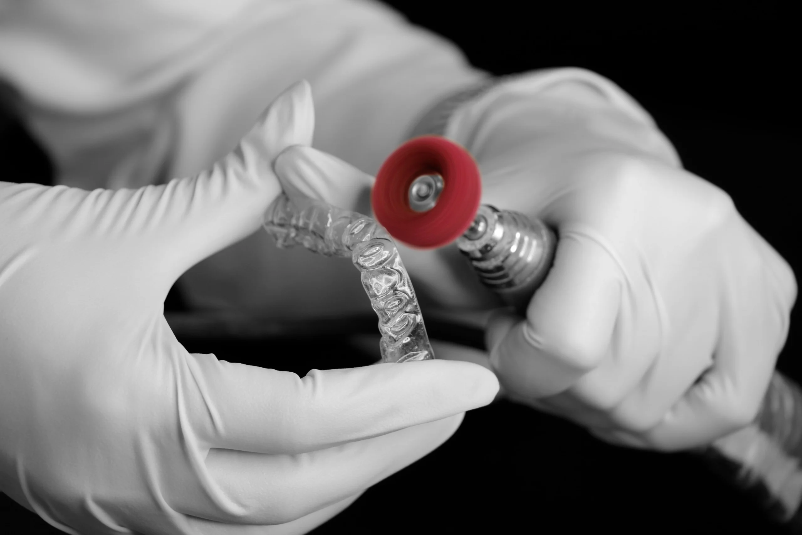 A dental technician polishing a clear plastic dental appliance with a grinding tool in a laboratory