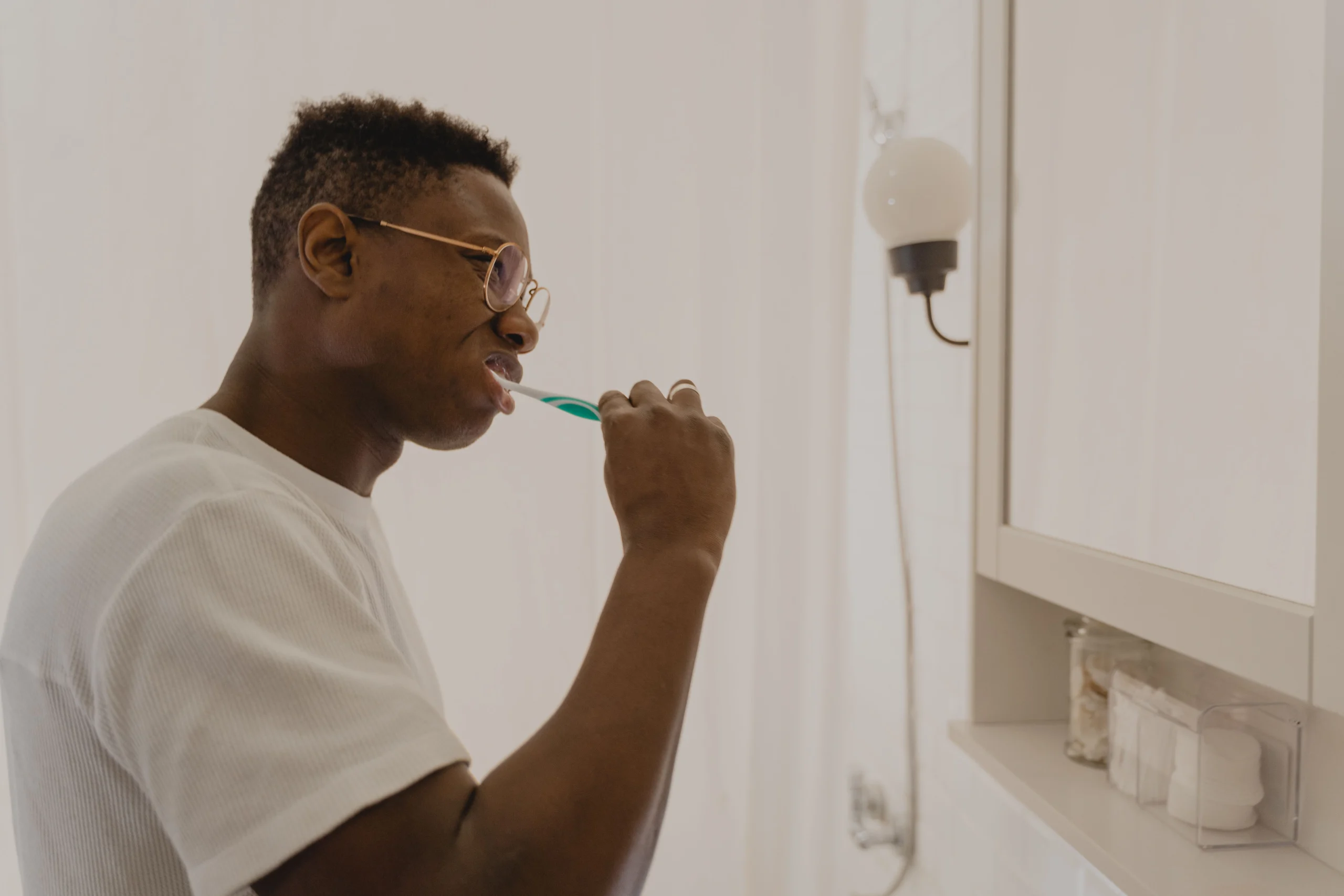 A man brushing his teeth at a bathroom sink as part of a daily oral care routine
